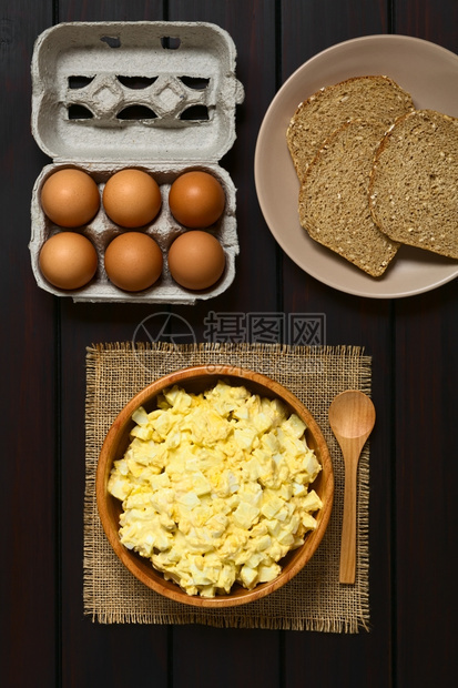 饮食调味品拍照土制新鲜鸡蛋沙拉配有木碗中的蛋和芥子酱上面还有鸡蛋箱和全谷物面包片用天然光照黑木头上方图片