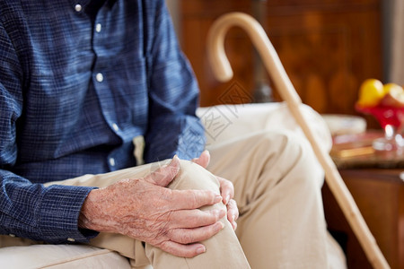 在室内高级的社会坐在索法家中因关节炎受膝腿疼痛而挨的近身老人背景图片
