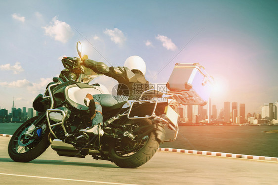 男子骑着摩托车在急速曲线上行驶用于旅和城市生活方式男子骑着摩托车乘坐直冲日落天空和城镇摩大楼高的快速曲线安全胎骑自行车图片