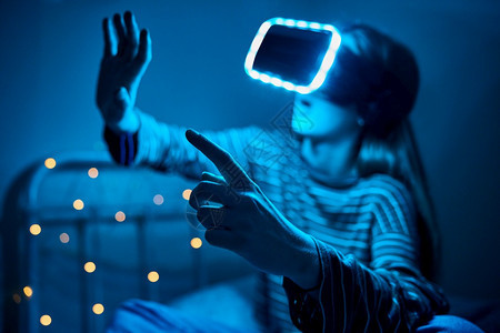 虚拟的游戏玩家夜里穿着虚拟现实头巾的床铺女青少年在家中玩视频游戏模拟器图片