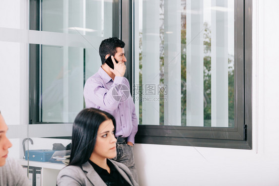 团队合作一名商人在办公室的窗口附近用手机说话在办公室的窗户旁边行政人员黑发图片