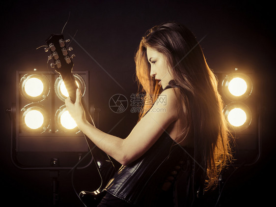 一位美丽的年轻女子在舞台灯前弹着电吉他的照片来自成人黑色的紧身胸衣图片
