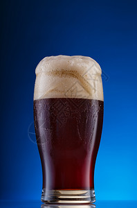 降低蓝色的背景上带有厚泡沫的深色精酿啤酒一杯蓝色背景上带有泡沫的深色精酿啤酒肥硕图片