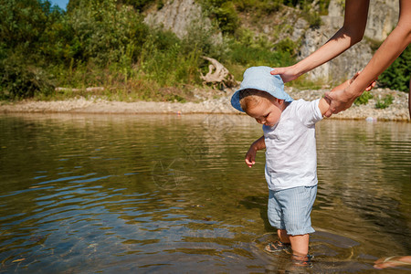 活动结石玩年轻母亲在阳光明媚的白天走在河水或湖边时抱着小男孩儿子图片