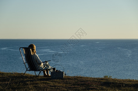 闲暇岛海洋坐在椅子上和篮坐着的女士在海边看着蓝图片