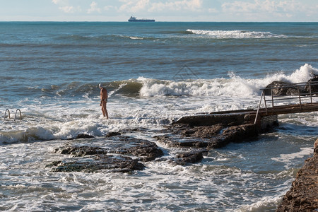 湿的波浪夏天有游泳帽的高级男子准备在粗海中游泳背景是货船图片
