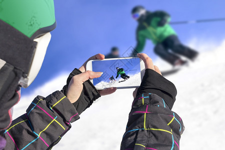 一名年轻女孩用手机拍摄滑雪者图片