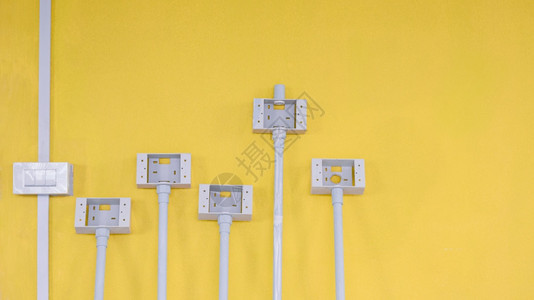 工业的漂浮白色塑料灯开关箱装有管道和电插的白塑料灯开关箱和在房屋建筑工地内黄色水泥墙壁背景上的电插座箱颜色图片