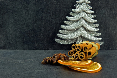 水平的肉桂棒星香两片橙子干和银圣诞树在黑暗的石头桌上地深浅的石板上作为圣诞装饰品关闭侧面最佳芳香图片