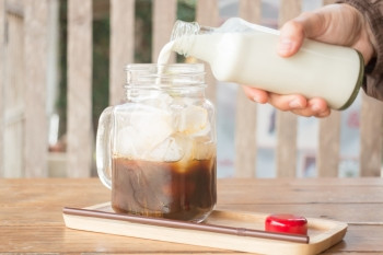 手瓶子挤牛奶到冰的咖啡杯股票照片糖图片