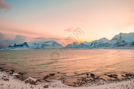 塞尼亚顶峰北欧的挪威冬季峡湾在清晨被雪积的山峰环绕粉红天空从太阳升起光反射在温冬峡湾的粉红色早晨水面上图片