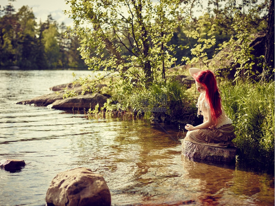 白种人吸引的独自迷年轻女子坐在岩石上做梦湖边过夏日图片