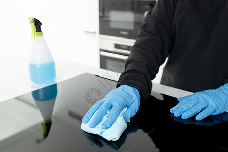 极简主义者手放在保护套上清洁现代电炉灶用最起码厨房的抹布擦洗蓝色工作图片