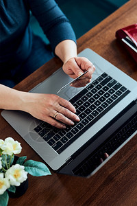 店铺妇女利用借记卡和膝上型计算机在线购物持有信用卡的手笔记本电脑键盘坐在办公桌从家里购买商品移动的互联网图片