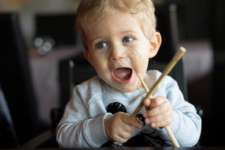 婴儿男孩坐在高椅子上餐馆用筷子玩耍白种人们眼睛图片