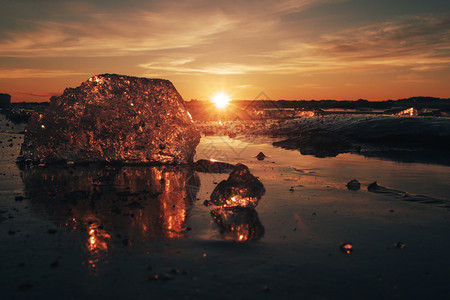 景观粉红色和琥珀颜的美丽透明冰块作为在日落时寒冷的海岸上闪耀珠宝海滨丰富多彩的图片