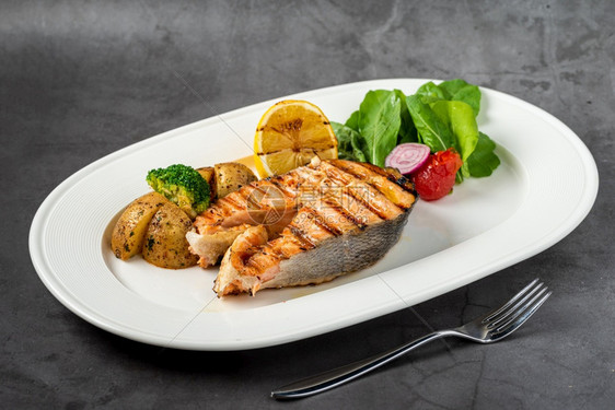 烤鲑鱼牛排和在黑石桌上的蔬菜鱼片盘子炙烤图片