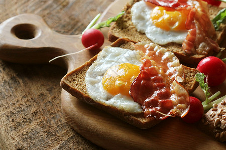 香脆的美国人烤培根炸鸡蛋和面包三明治早餐在切菜板上吃煮餐桌烤培肉煎鸡蛋和面包三明治早餐在切菜板上吃准备好的图片
