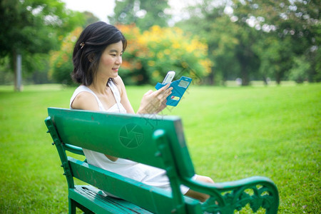 在公园使用移动智能手机的亚裔妇女自然电话聪明的图片