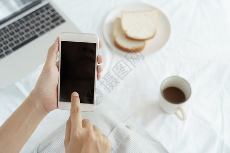 工作妇女手握并用智能电话在办公桌背景上持有和使用智能手机的在桌上有咖啡面包和笔记本电脑空白的公司成人图片