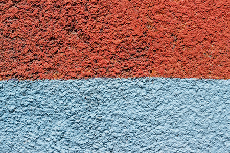 粗糙的颜色蓝混凝土墙碎片涂有橙色和蓝油漆一半作为背景或纹理图片