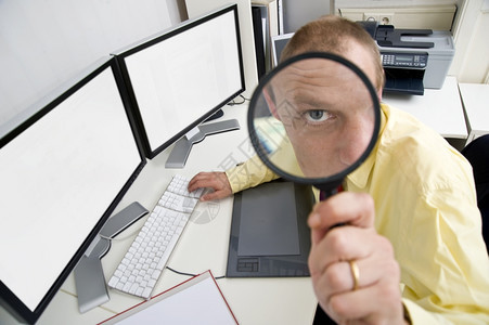 一个商人的眼睛坐在双屏幕电脑的背后通过放大镜看到一个商人的眼睛这说明他小心监视和敏锐地从事商业活动一种逃脱手图片
