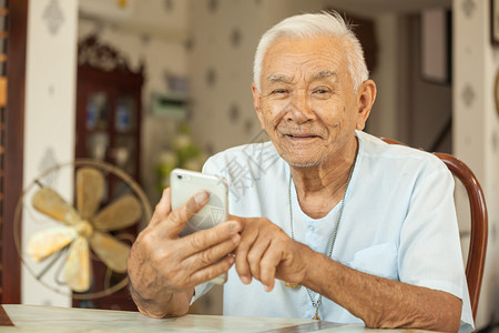 坐在客厅桌子上玩手机的老年人图片