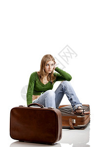 坐着的优雅在床上美丽年轻女子带着两个旧皮手提箱在门外等待着包图片