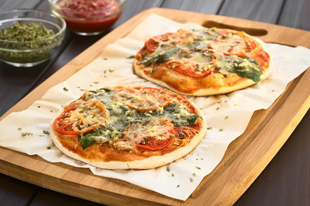 自然蔬菜木板上烤纸的自制菠菜和番茄披萨用天然光聚焦点在暗木上拍照第一张披萨的焦点是三分之一烘烤图片