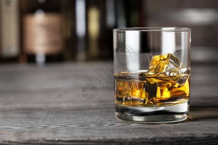 威士忌杯子酒上加冰在露台拍摄以模糊的背景威士忌杯子和冰在露台木制的头寒冷图片