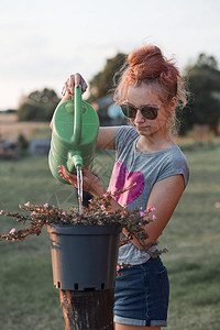 自然绿色帮助为花盆里种植的鲜浇水从绿罐中倒在日落Candid人后院工作真实时刻和情况提供饮用水的少女孩子图片