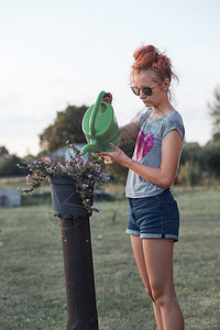 天园丁帮助为花盆里种植的鲜浇水从绿罐中倒在日落Candid人后院工作真实时刻和情况提供饮用水的少女孩图片