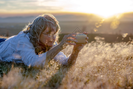女人躺在干草中日落时用自然智能手机拍照片女士旅游移动的图片