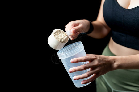 服务锻炼酪蛋白近距离接女测量一勺威氏蛋白质和摇晃瓶制作蛋白奶昔图片
