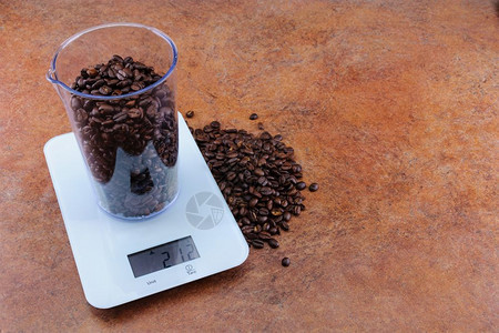 过程产品重量为50毫升其重量为21克部分产品位于台式桌面上与比例尺相靠的Coffe在电子尺度上的一个测量杯子上有一个复制空间产品图片