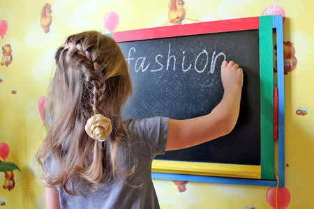 美丽的辫子漂亮女孩在黑板上写字时尚辫子漂亮的女孩在家里黑板上写字时尚玩童年图片