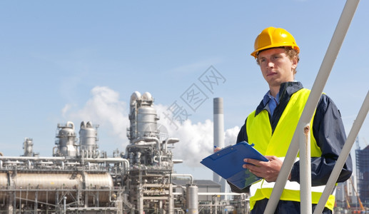 化石在工厂和炼油前面戴硬帽和安全背心的年轻主管手拿着纸巾板和笔身着硬帽子和安全背心男人难的图片
