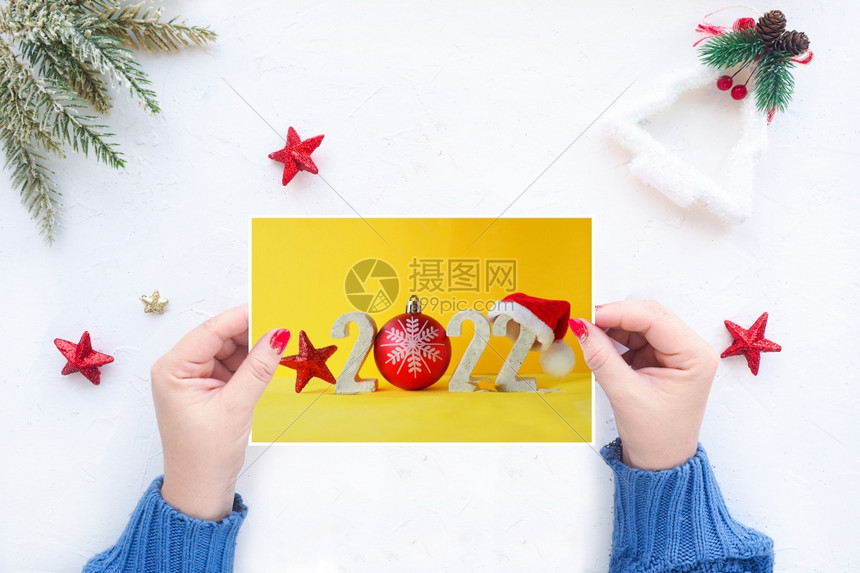 祝贺玩具毛衣女用手拿着圣诞贺卡在带有圣诞装饰品的白桌背景上举着圣诞贺卡图片