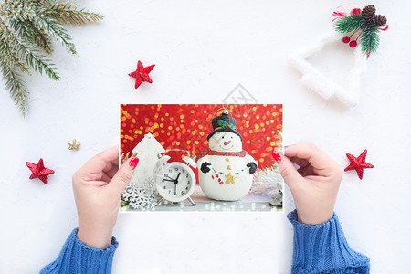 桌子相片礼物女用手拿着圣诞贺卡在带有圣诞装饰品的白桌背景上举着圣诞贺卡图片
