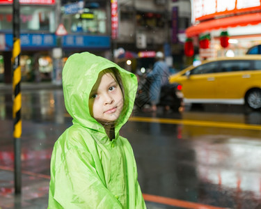 外套穿着绿色雨衣在市街旁边淋雨的年轻女孩快乐趣图片