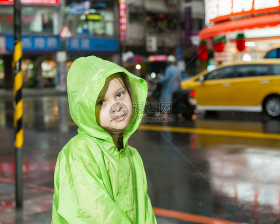 外套穿着绿色雨衣在市街旁边淋雨的年轻女孩快乐趣图片