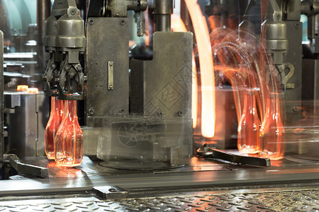 温度工厂团体热玻璃瓶红色子沿着玻璃厂ToningConveyor的传送台移动装有热玻璃瓶图片