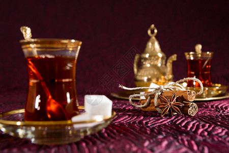 传统玻璃中土耳其茶与八角和肉桂条的特写传统玻璃中土耳其茶饮料金的盘子图片