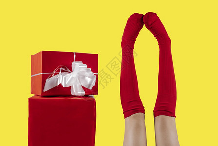 假期黄色背景的红礼物旁边贴着红色袜子的腿和色袜子女孩图片