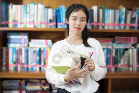 在书架前抱着书的亚洲女学生图片