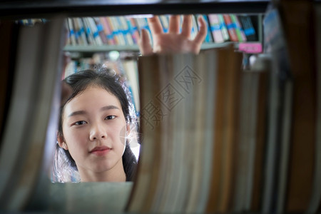 在图书馆书架上搜寻书籍的亚洲女学生图片