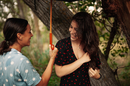 外部两名年轻妇女在田地上拿着雨伞站在身裙子和运动鞋的树丛中站立微笑年轻的图片