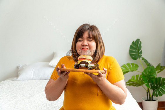 思维快速地胖的饥饿超重年轻亚洲女人拿着汉堡包她饿了所有的时间和过量吃饱谷食和狂她的生活方式正在吃快餐所有时间不健康的概念图片
