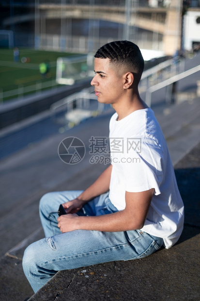 空的坐着一个穿T恤衫和牛仔裤的英俊男子独自坐在体育场的运动台成人图片