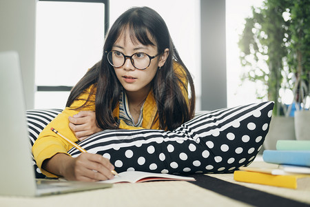 趴在抱枕上用笔记本电脑在线学习的女孩图片